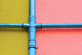 Deux tuyaus bleus se croisant sur un mur coloré
